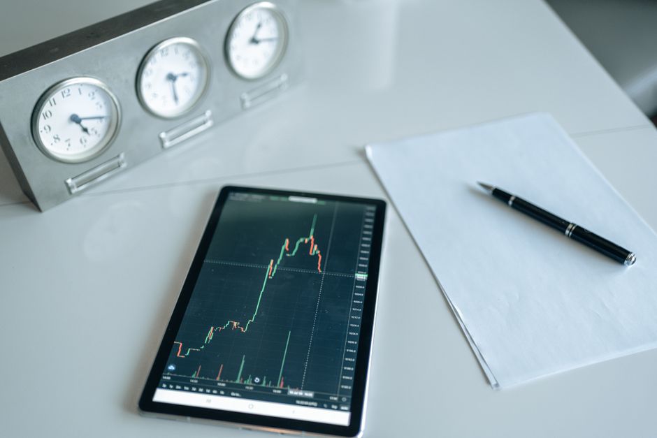 Tablet with stock market chart on a desk with clocks and pen.